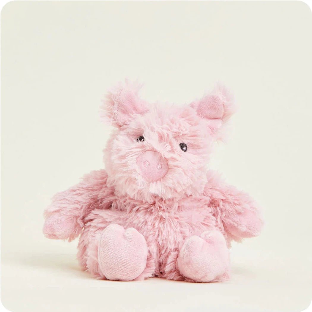 A front view of the Warmies Pig Junior plush toy with a soft pink color and heart-shaped feet against a plain white background.