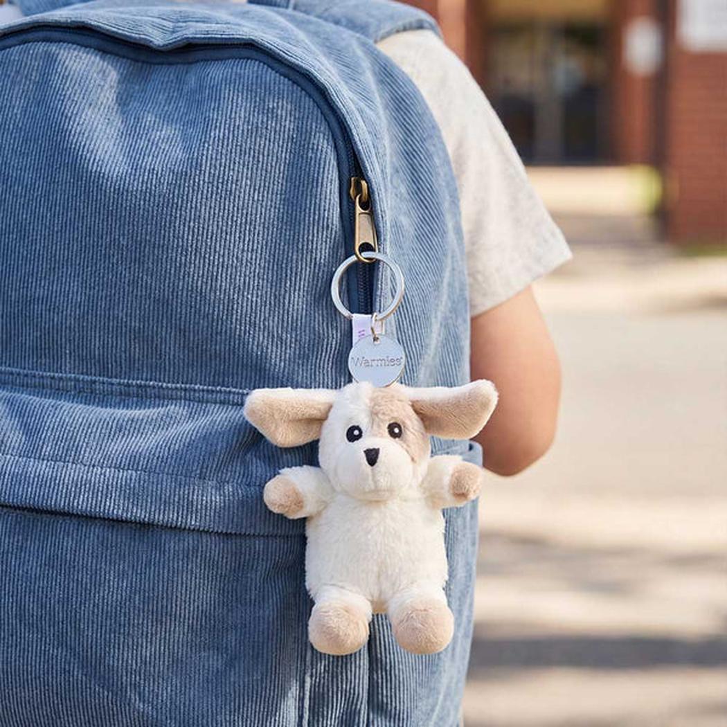 Back of a person wearing a blue corduroy backpack with a Warmies Puppy Keyring attached to the zipper.