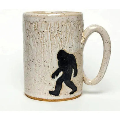 A white ceramic mug with a black Sasquatch design and a speckled finish, shown from the front with a plain white background.