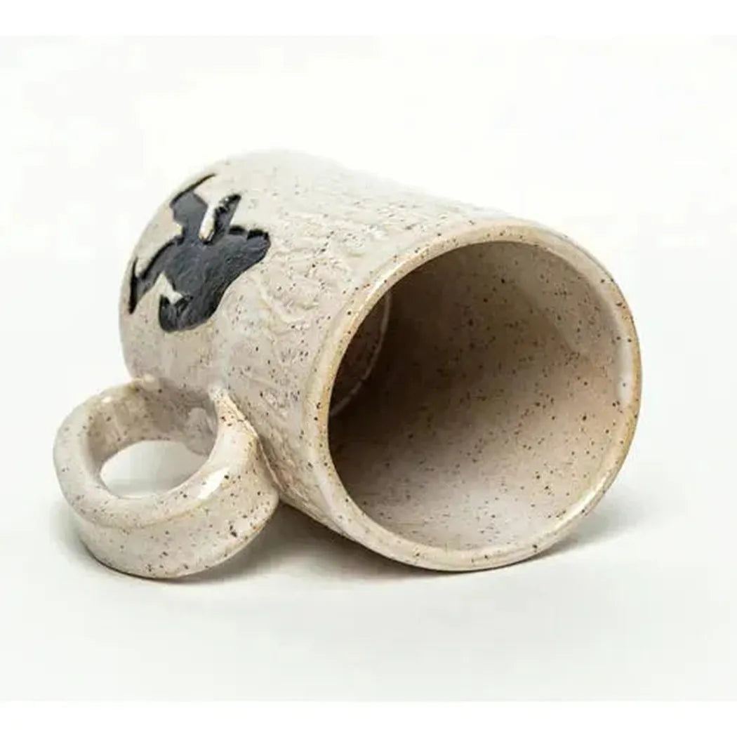A side view of the White Squirrel Clayworks Sasquatch / Bigfoot Handmade in Ohio Ceramic White 14oz Mug lying on its side against a white background.