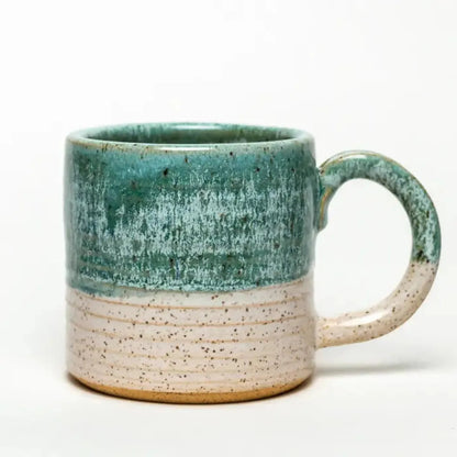 A front view of the White Squirrel Clayworks Turquoise Hand-Thrown Ceramic 12-14 oz Mug with a two-tone turquoise and speckled beige design against a white background.