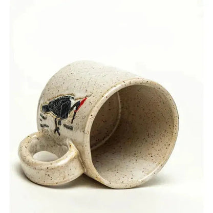 A side view of the White Squirrel Clayworks Woodpecker Design Handmade Ceramic White 10oz Mug showing the bird design and speckled texture against a white background.