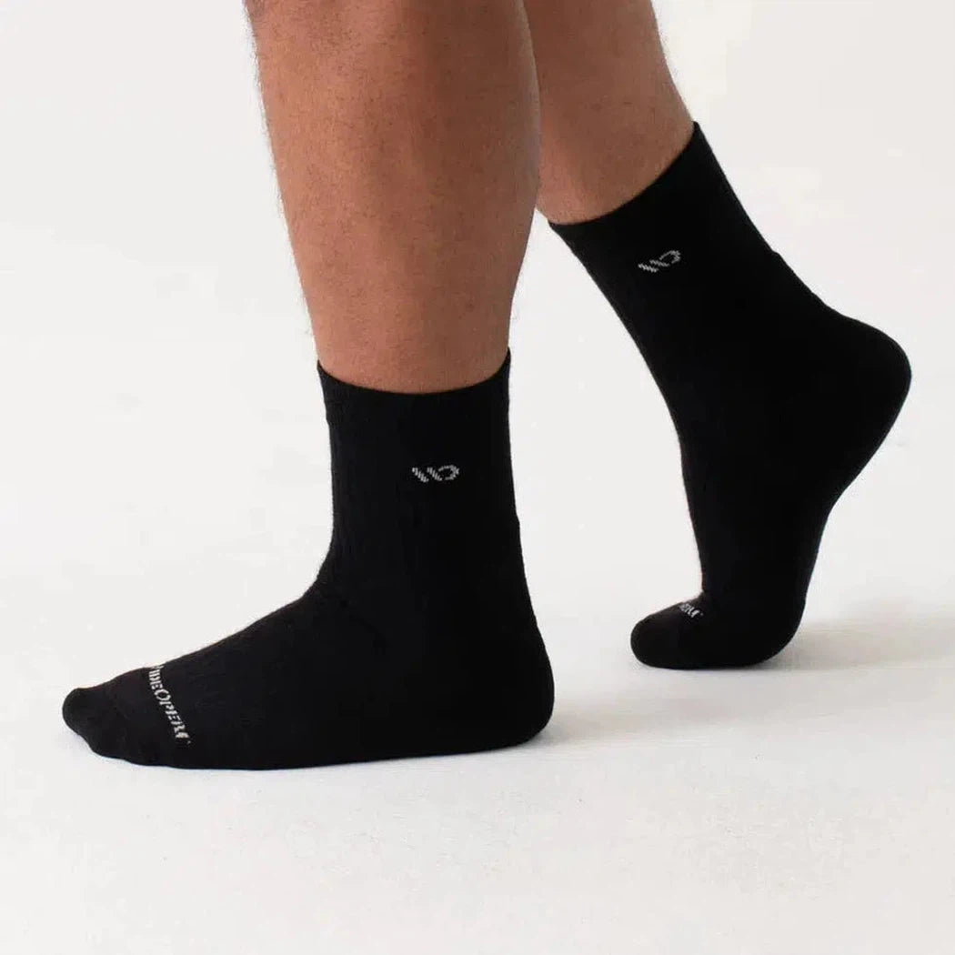 A close-up of a man wearing black Wide Open Men's Solid Cushioned Micro Crew Socks against a white background.