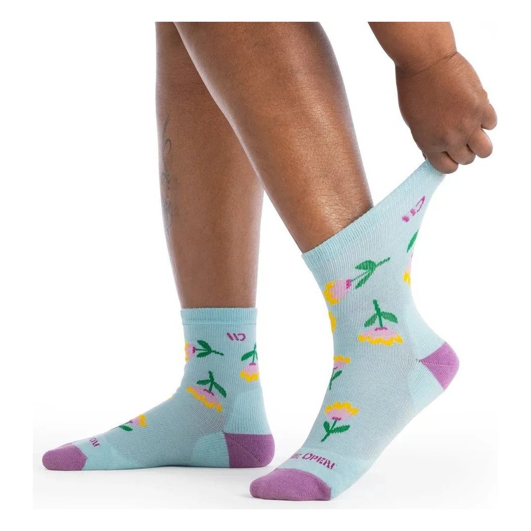 A person wearing light blue Tulip Purple Wide Open Women's Full Bloom Cushioned Micro Crew Socks with floral designs and purple toes, showing the socks from a side angle against a white background.