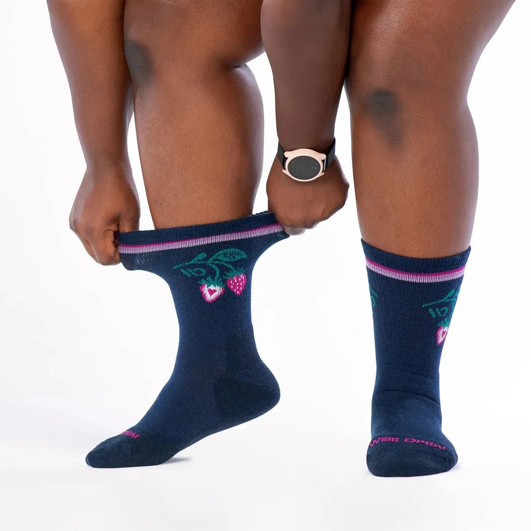 A model wearing Wide Open Women's Strawberry Patch Crew Midweight Cushion Socks in Eclipse shows the strawberry design and midweight cushioning against a white background.