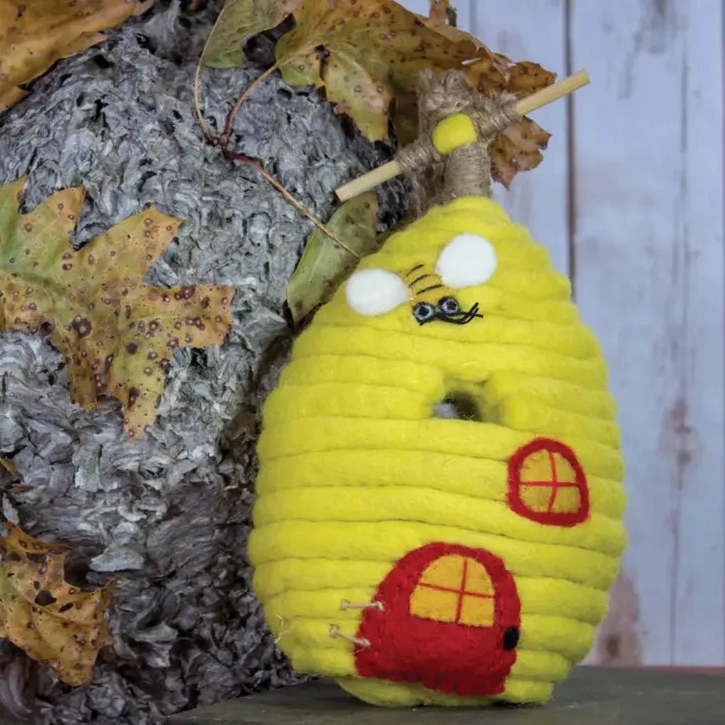 A yellow Wild Woolies Honey House Birdhouse with red doors and windows sits against a textured charcoal background.