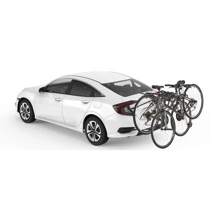 A white sedan with a Yakima HangOut car rack holding two bicycles is shown from a rear three-quarter angle against a plain white background.