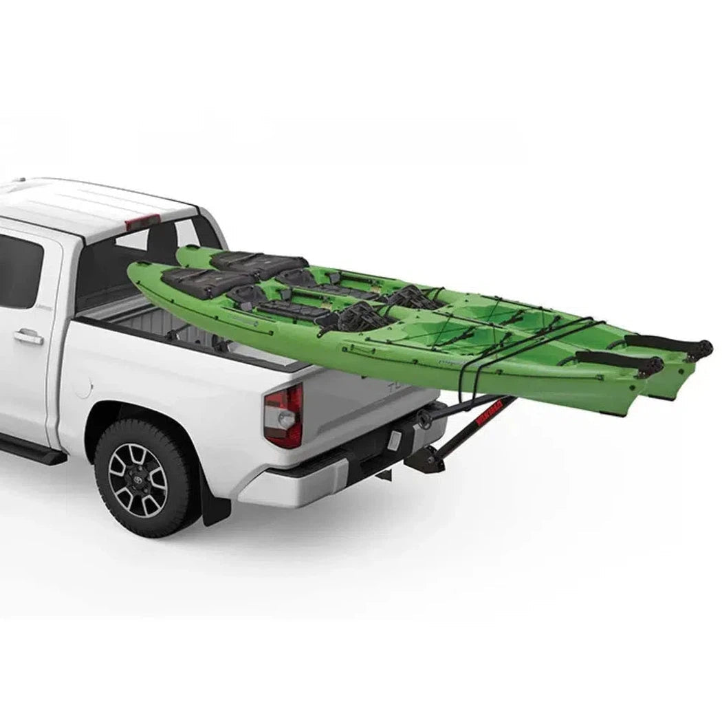A white truck with a Yakima LongArm rack system carrying a green kayak in its bed, viewed from the rear.
