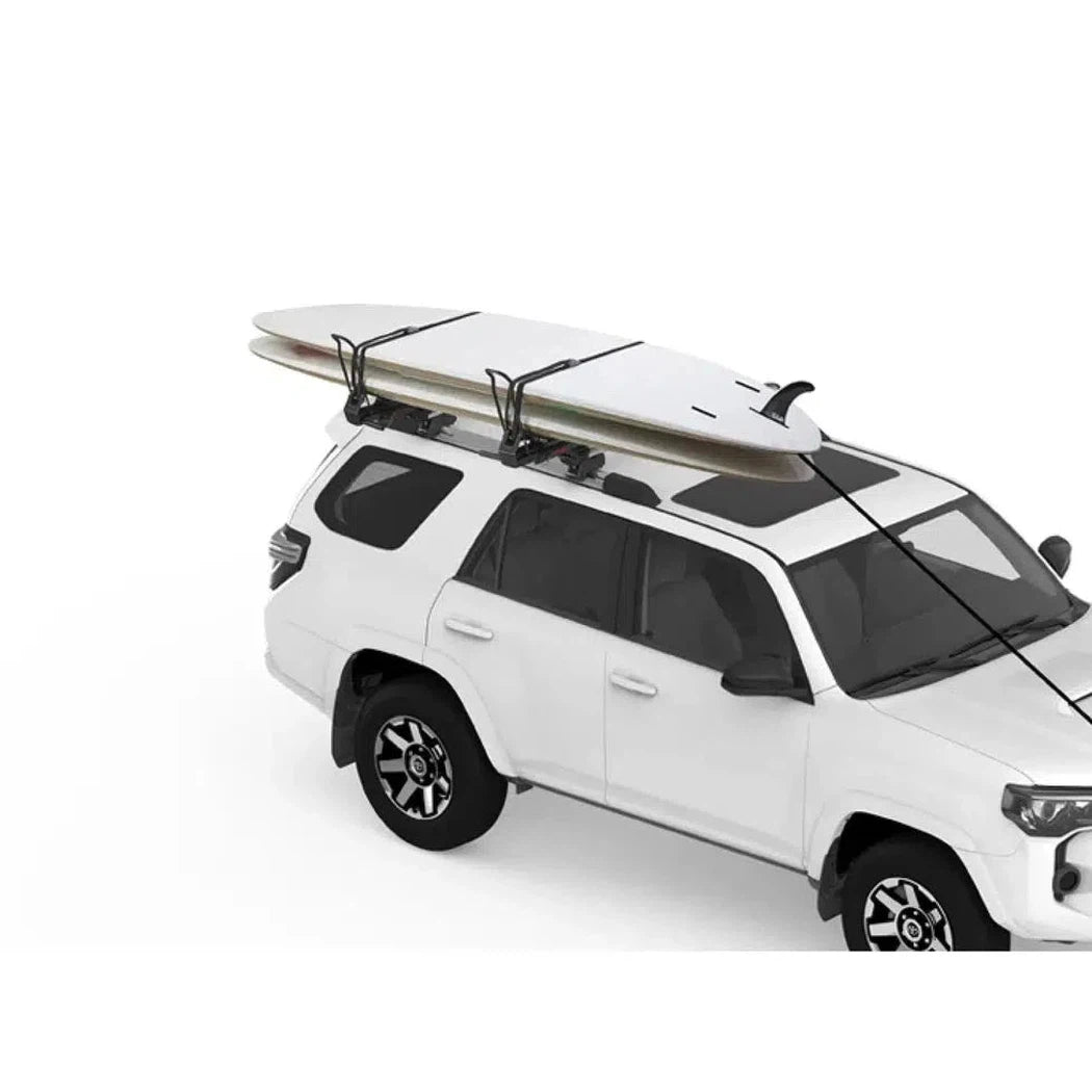 A white SUV with a Yakima Showdown car rack holding a surfboard, photographed from a slightly low angle against a plain white background.