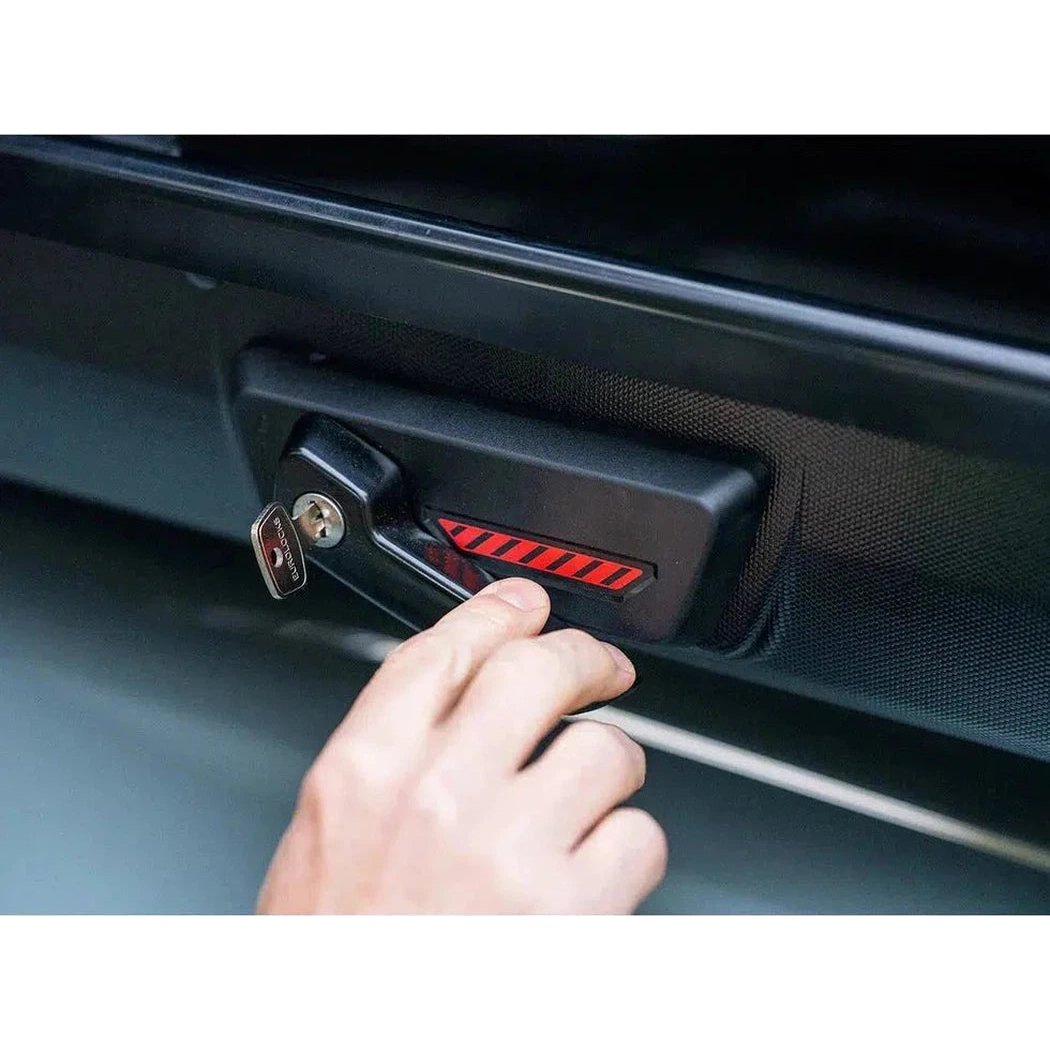 A hand inserts a key into the lock of a Yakima SkyBox NX 18 cargo carrier mounted on a vehicle door.