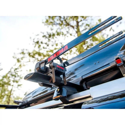 A Yakima Wheelhouse car rack system mounted on a dark blue vehicle with trees in the background.